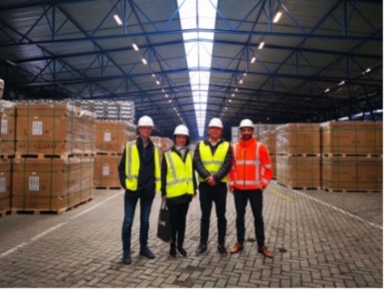 Four people wearing hard hats and high-visibility clothing in a warehouse