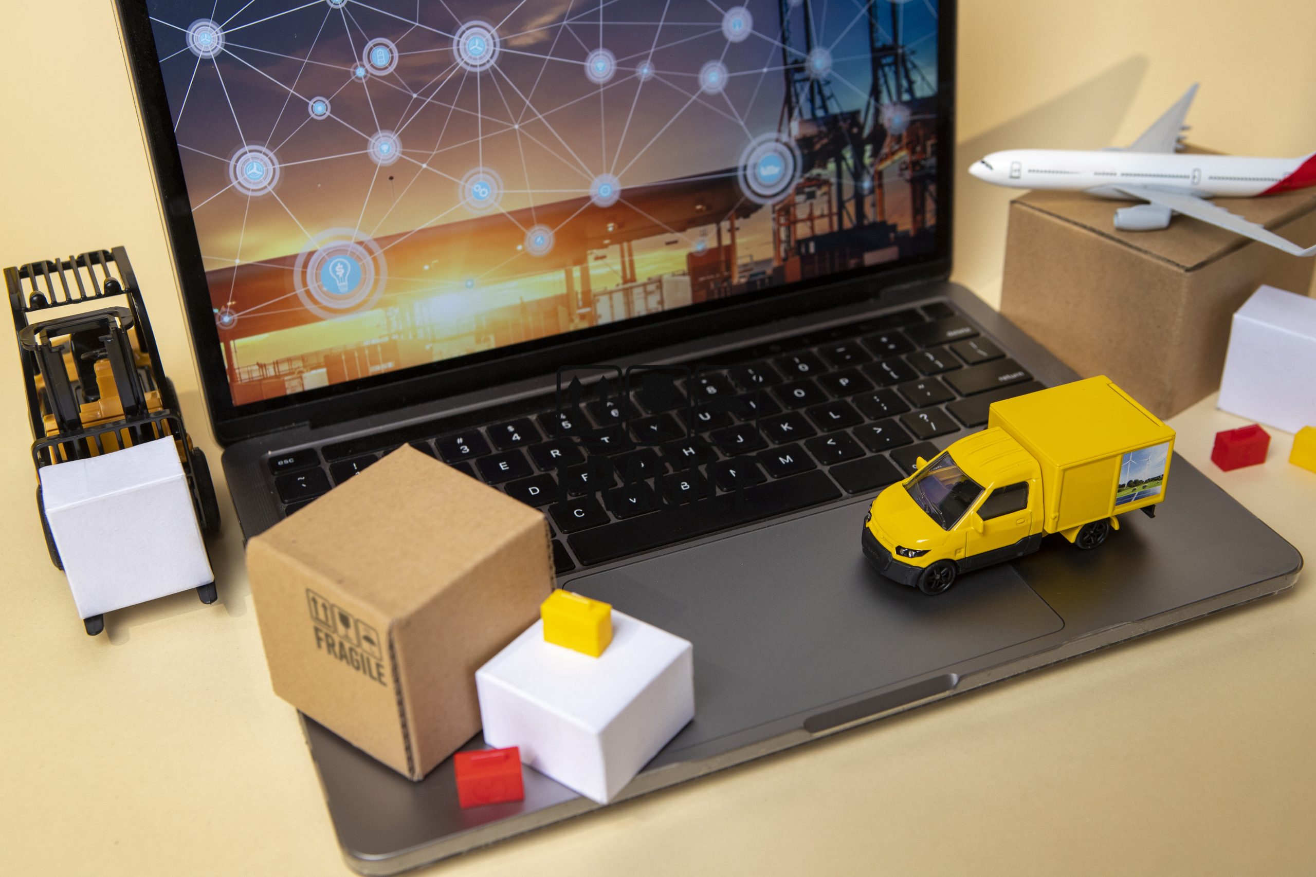 Laptop with a supply chain diagram beside model transport vehicles and parcels